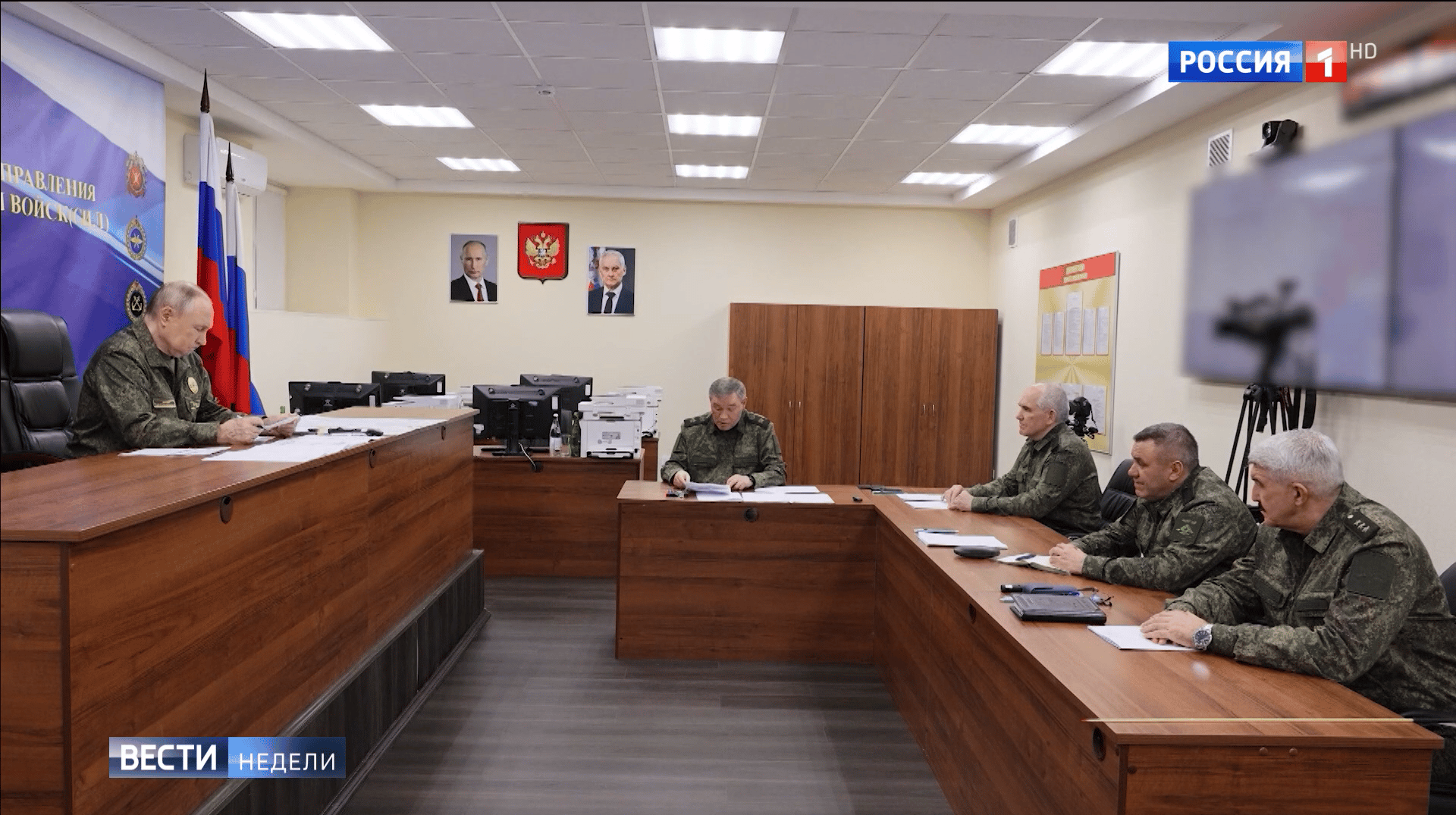 Putin w mundurze siedzi przy biurku na podwyższeniu. naprzeciw niego przy niższych biurkach siedzą wojskowi