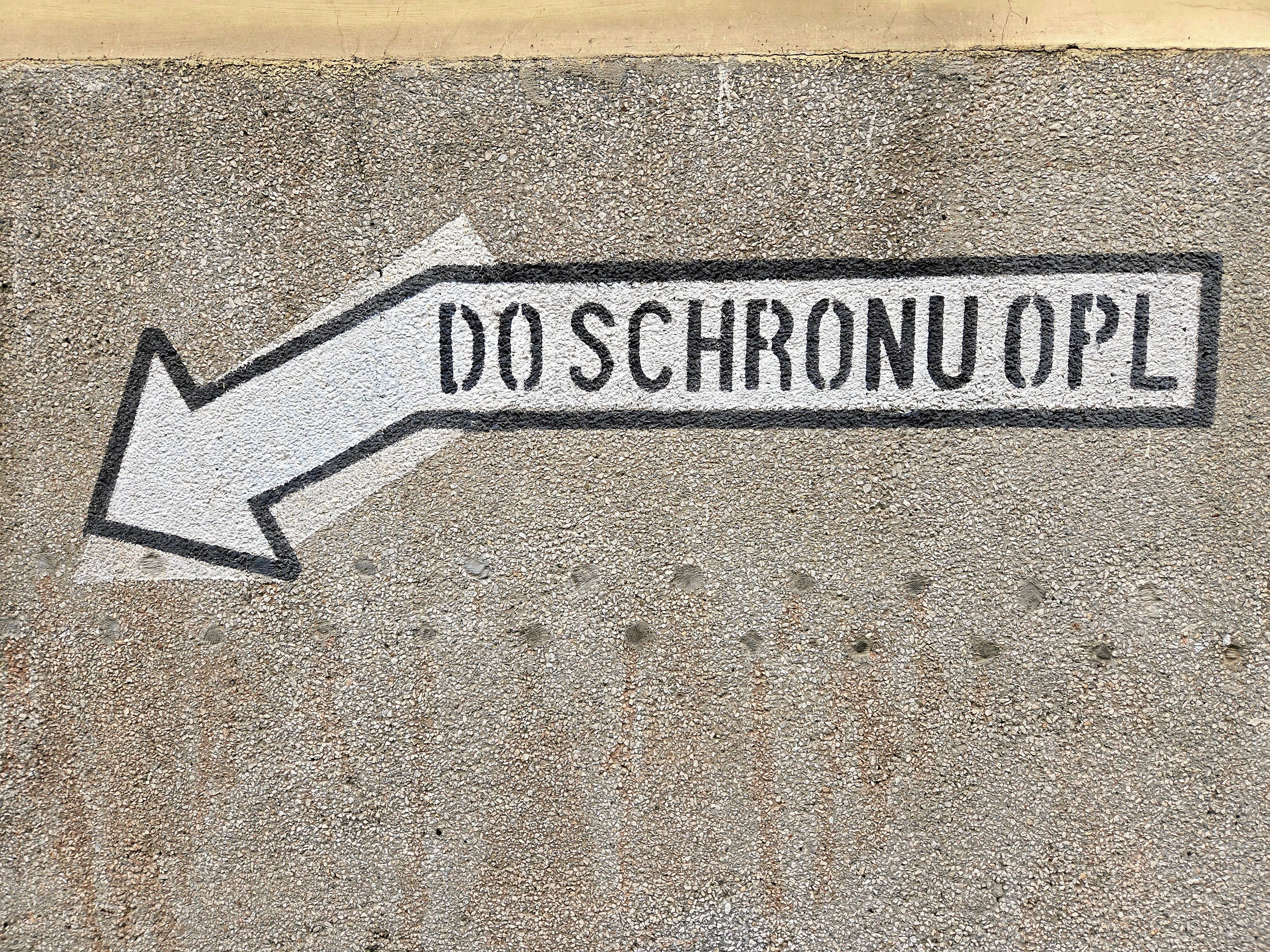 Napis na ścianie Do schronu opatrzony białą strzałką, wskazującą kierunek