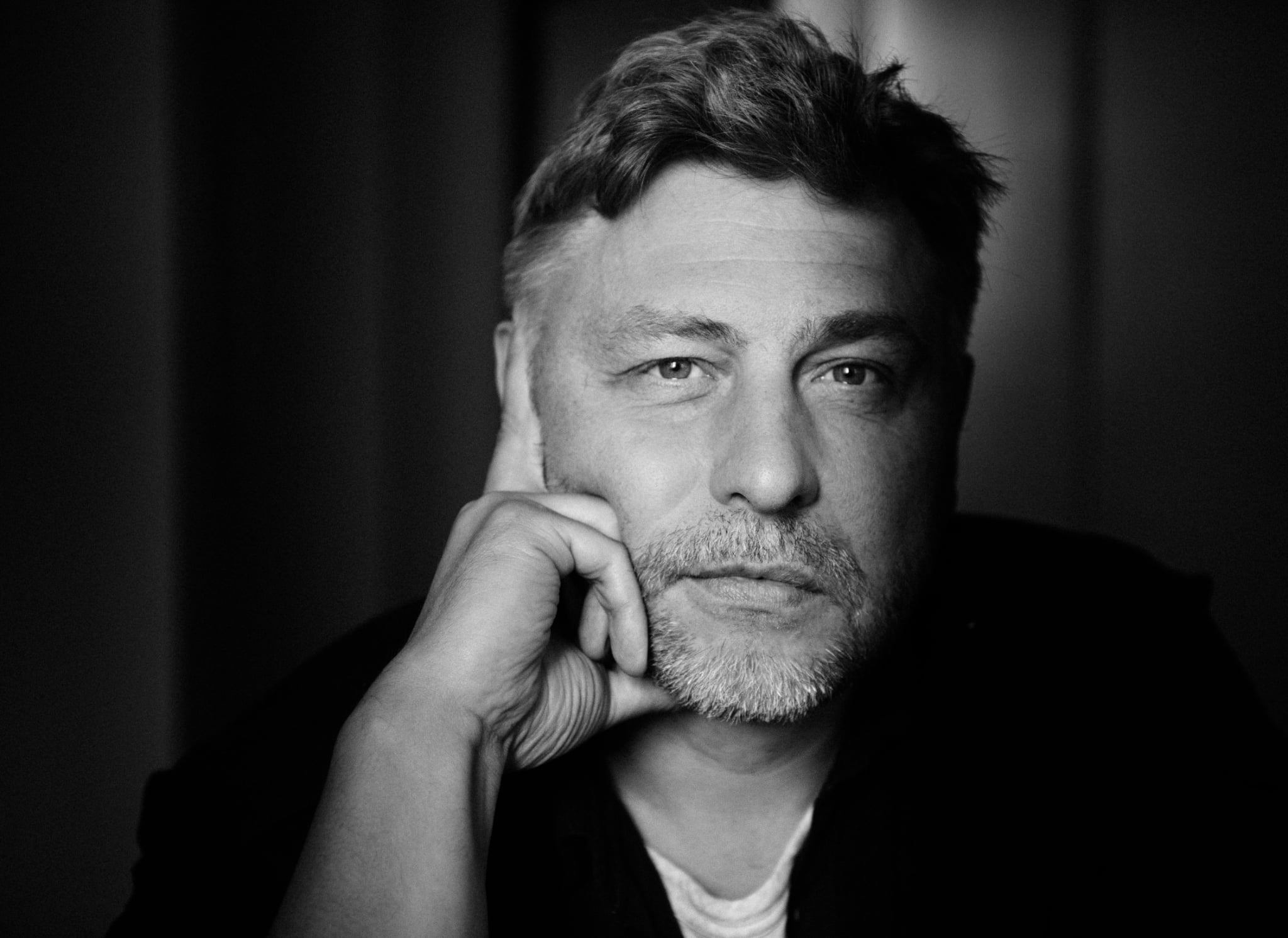 Czarnobiałe zdjęcie mężczyzny, który patrzy w kamerę podpierając głowę prawą ręką