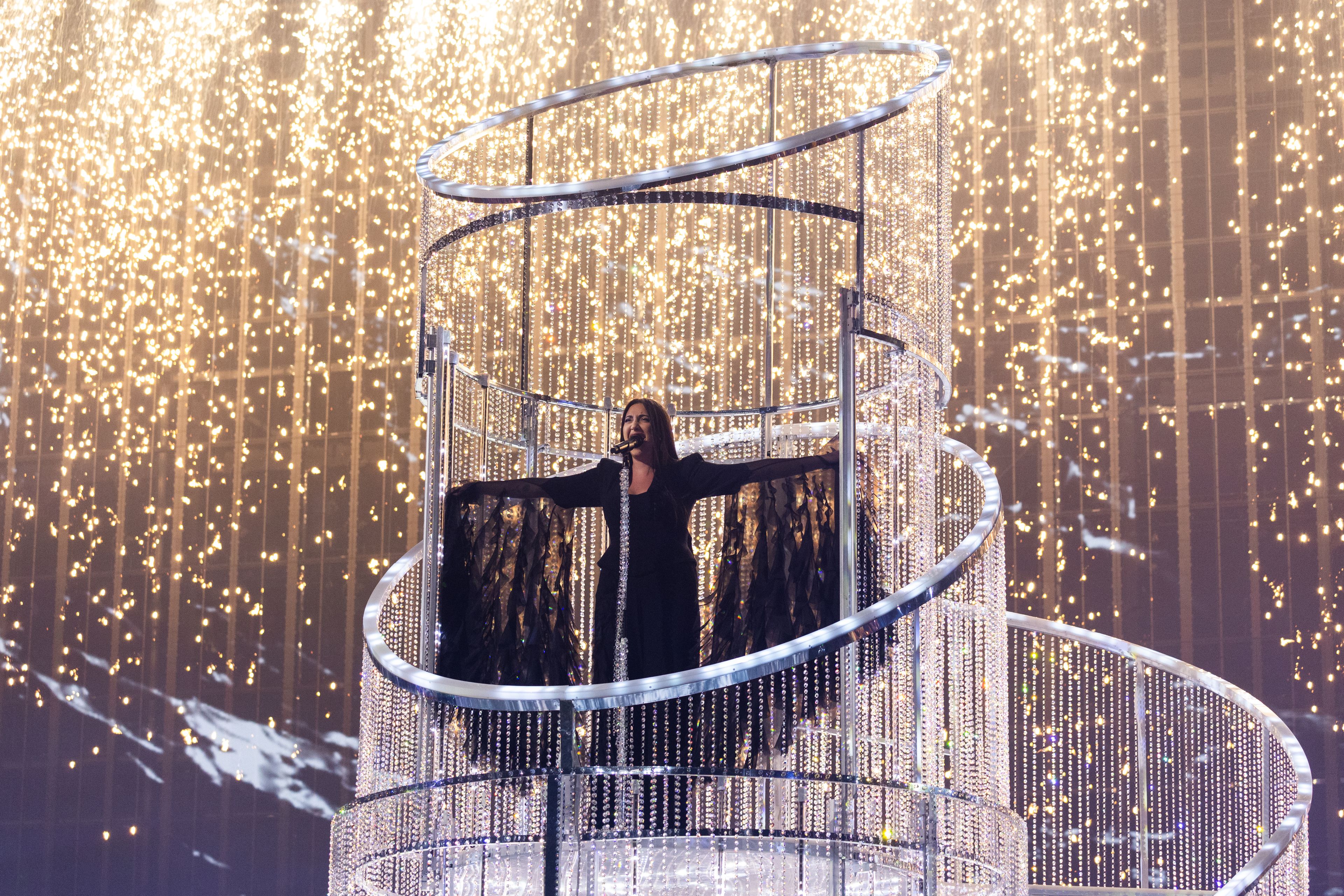 wokalistka stoi na platformie na scenie, za nią sztuczne ognie