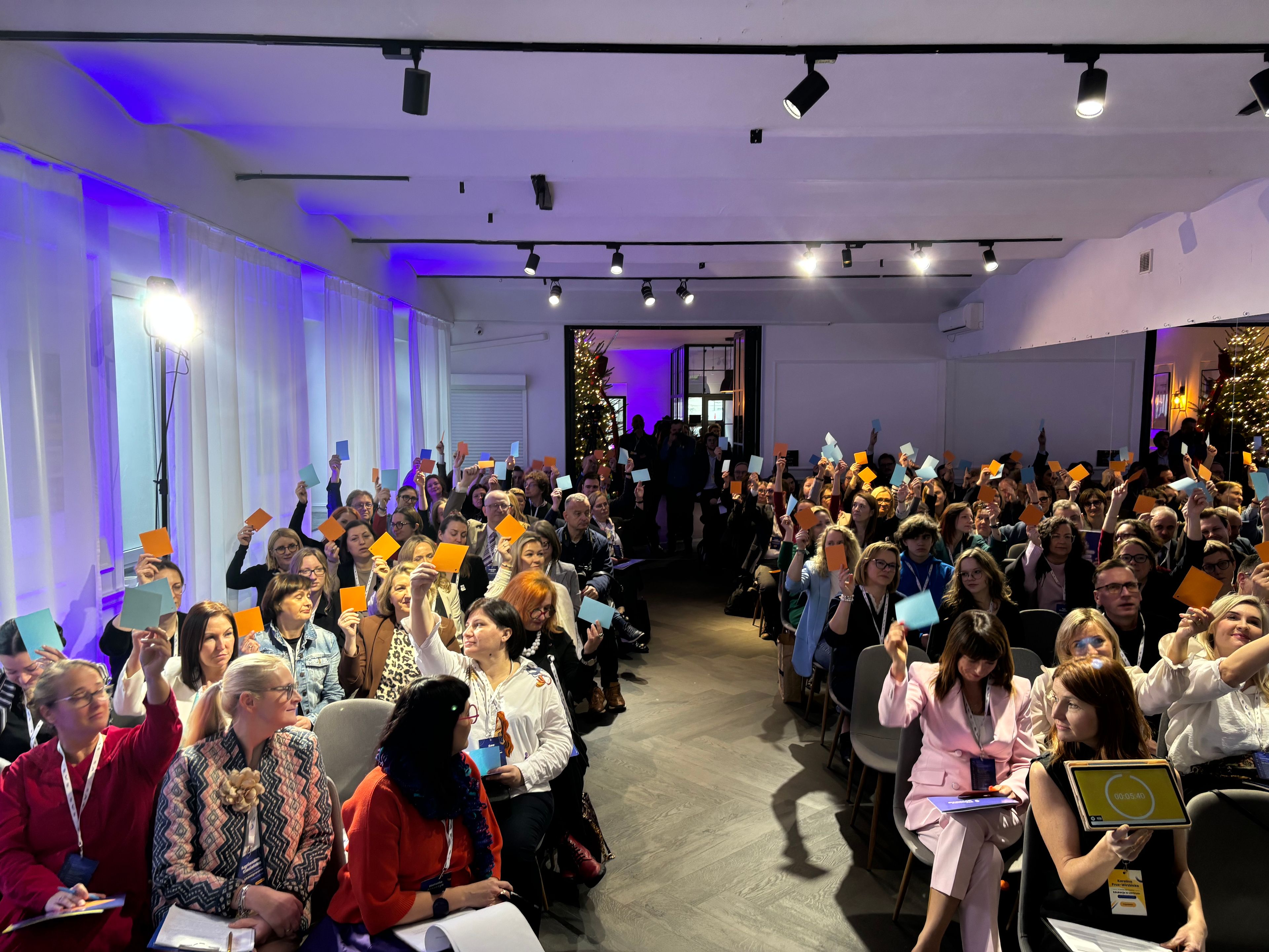 Pełna sala osób podnoszących niebieskie i pomarańczowe kartki