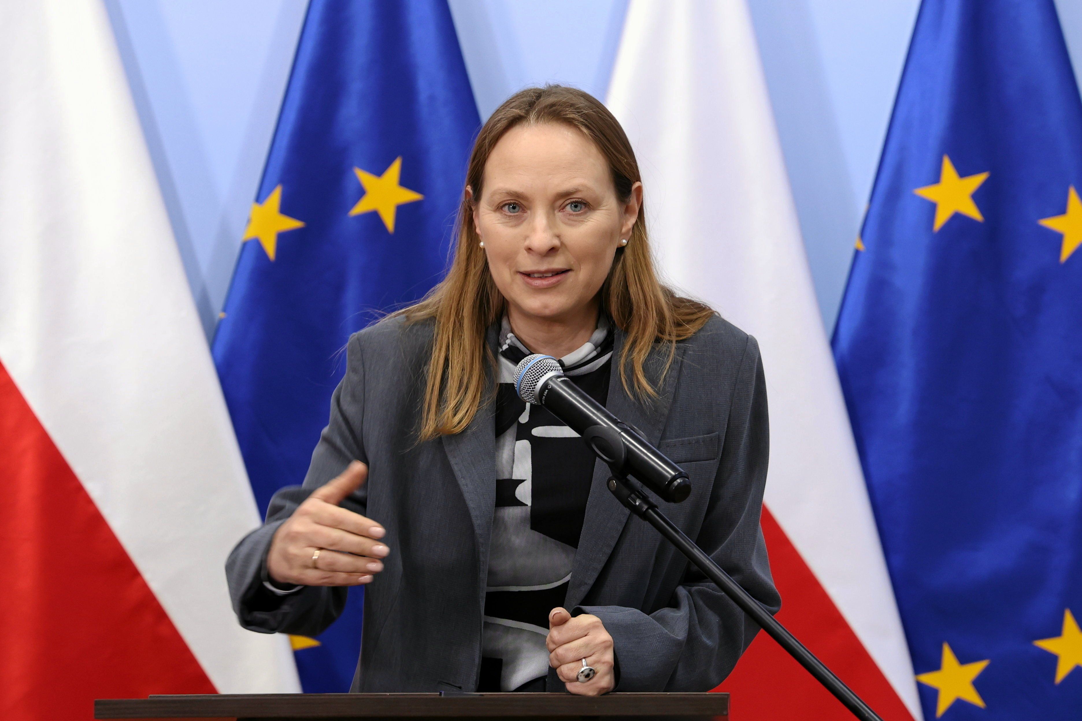 Katarzyna-Pełczyńska Nałęcz nachylona nad mikrofonem, w tle flagi UE i Polski