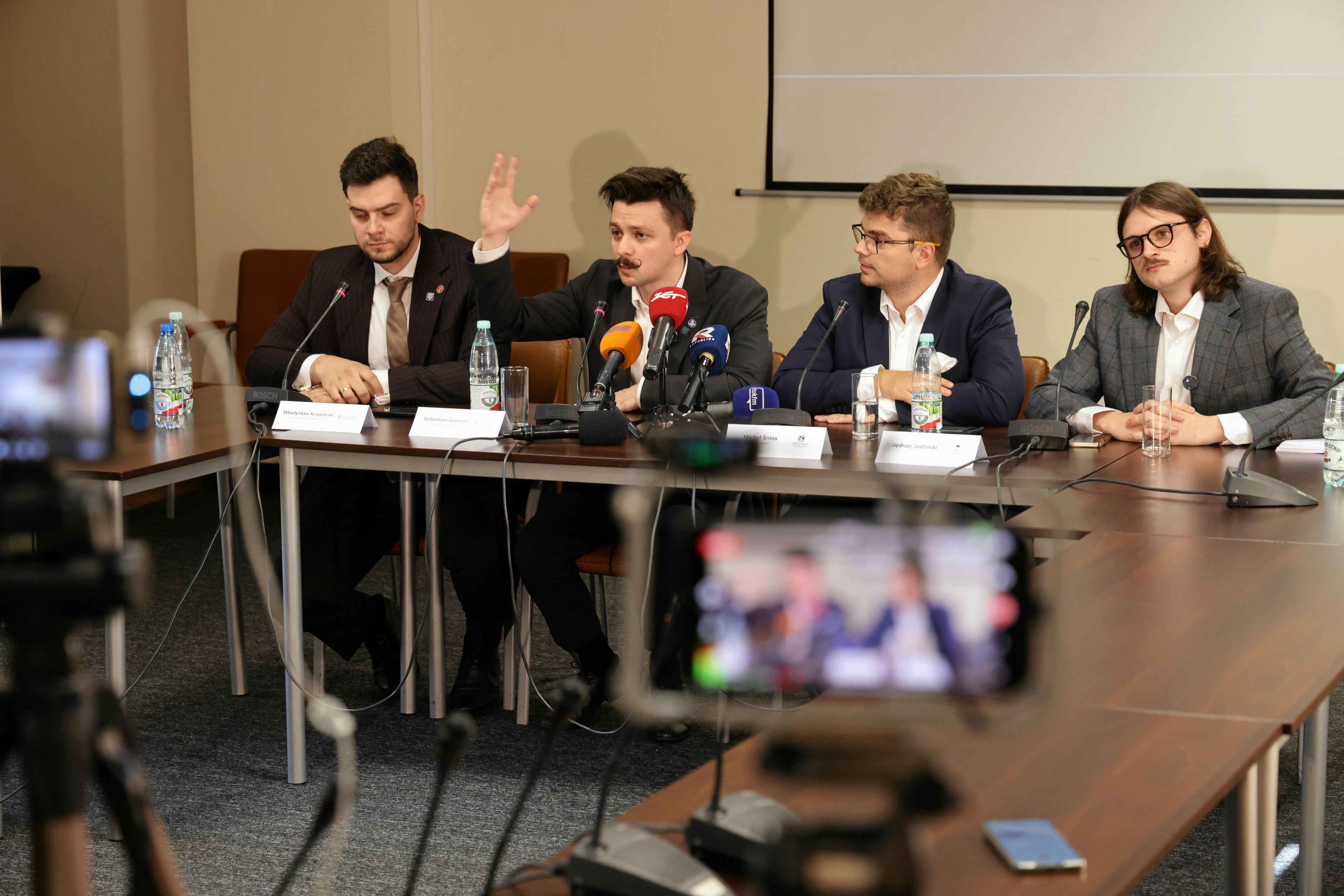 Czterech mężczyzn w garniturach na konferencji prasowej