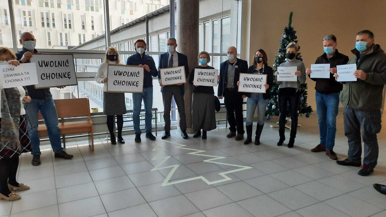 kilka osób stoi wokół obrysu choinki na podłodze, trzzymają w rękach banery "Uwolnić choinkę"