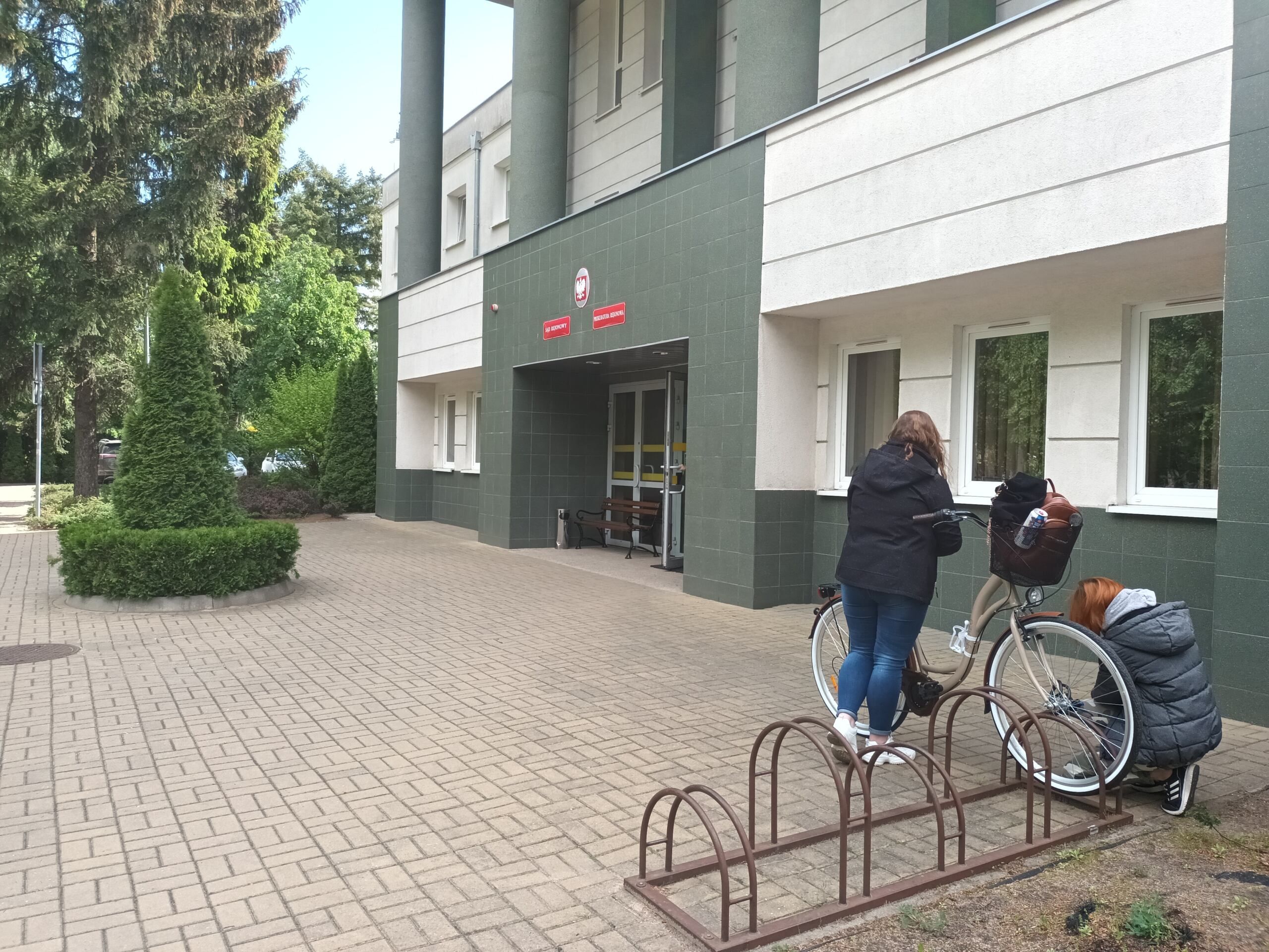 Dwie kobiety odpinają rower pod budynkiem sądu