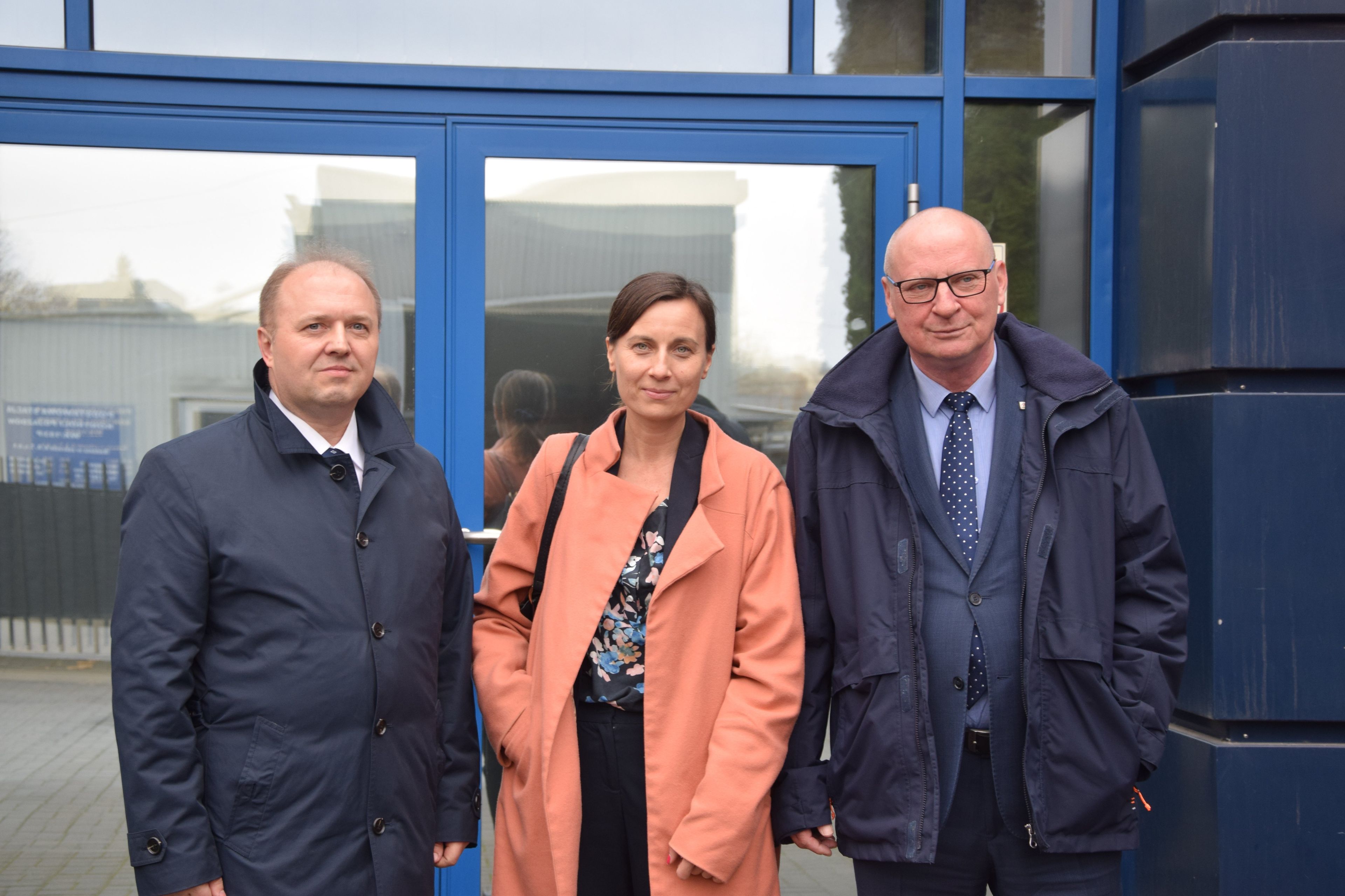 Dwaj mężczyźni i kobieta pozują do zdjęcia przed wejściem do budynku 