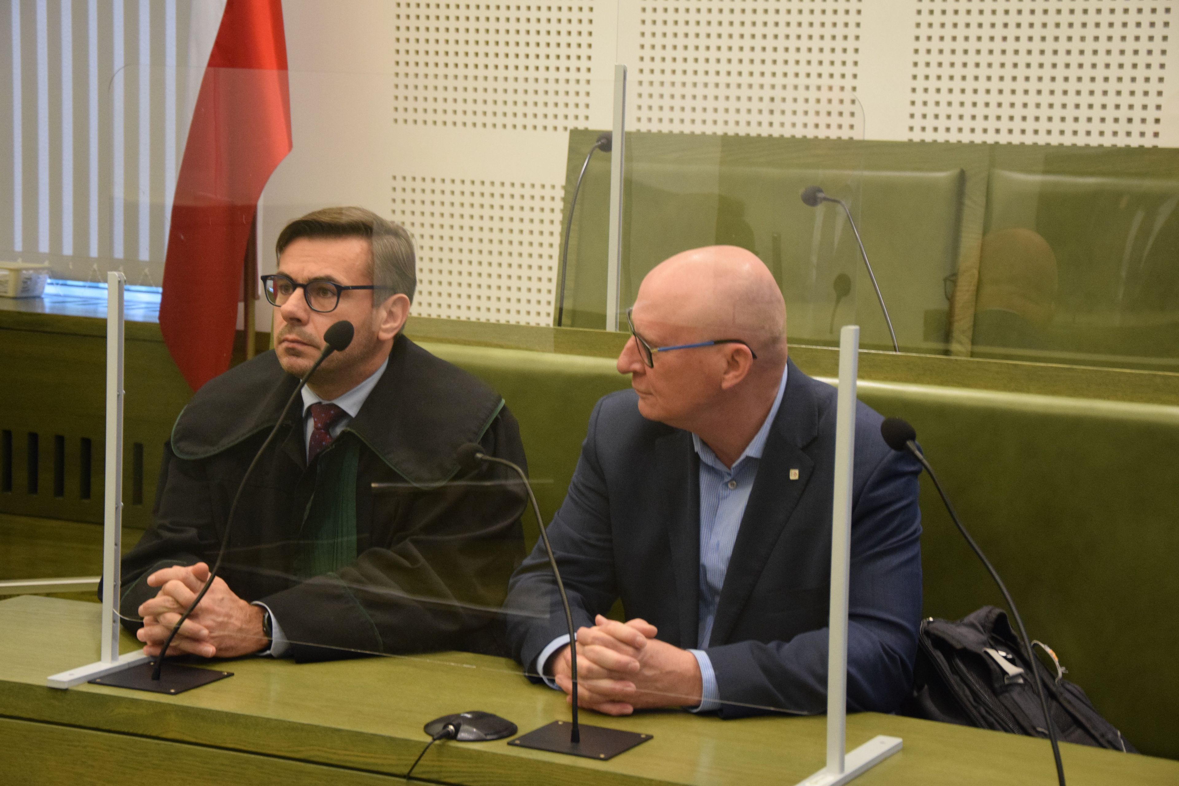 Mężczyzna w todze adwokackiej i mężczyzna w garniturze siedzą w sądzie