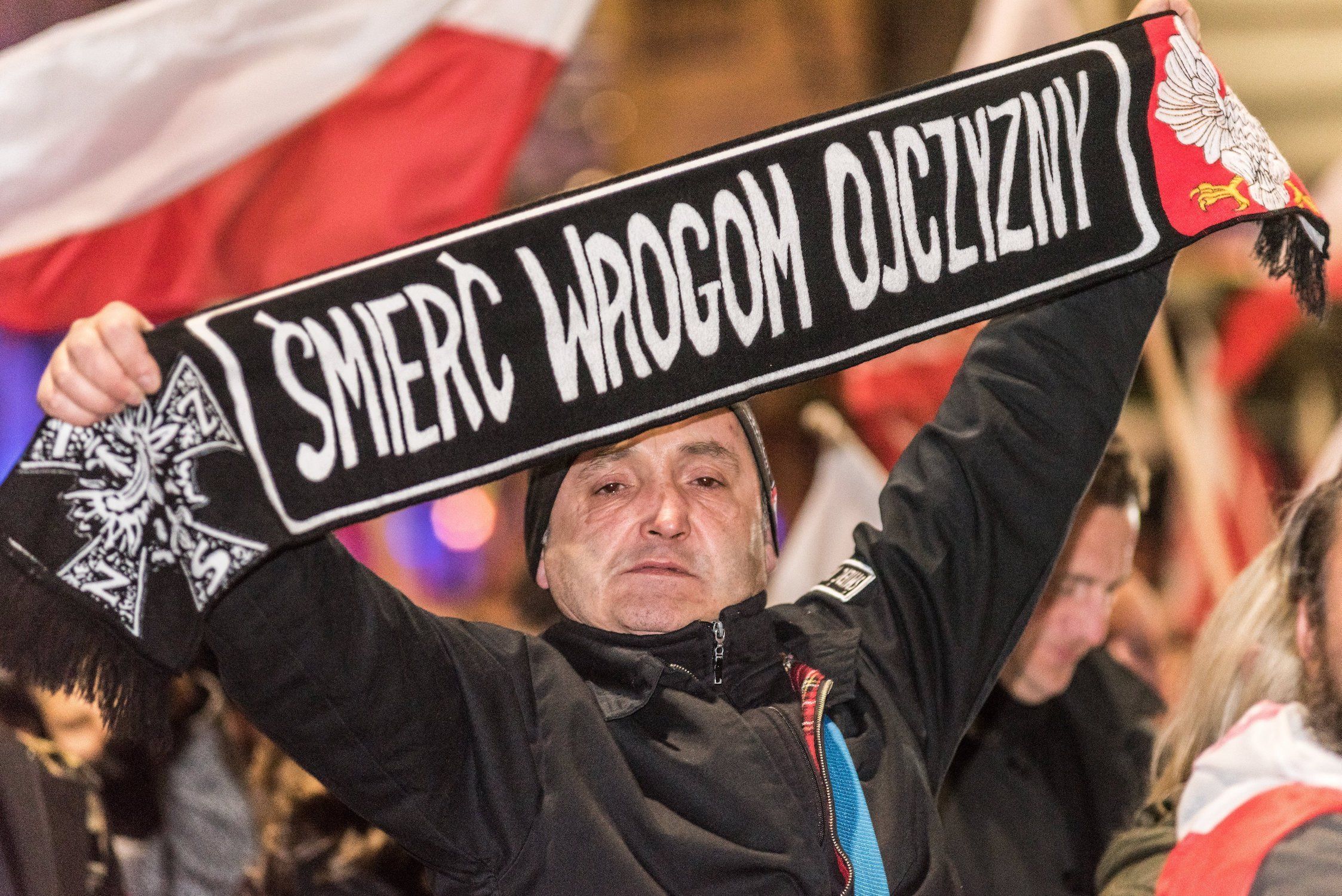 Mężczyzna trzyma szalik z napisem "Śmierć wrogom ojczyzny"