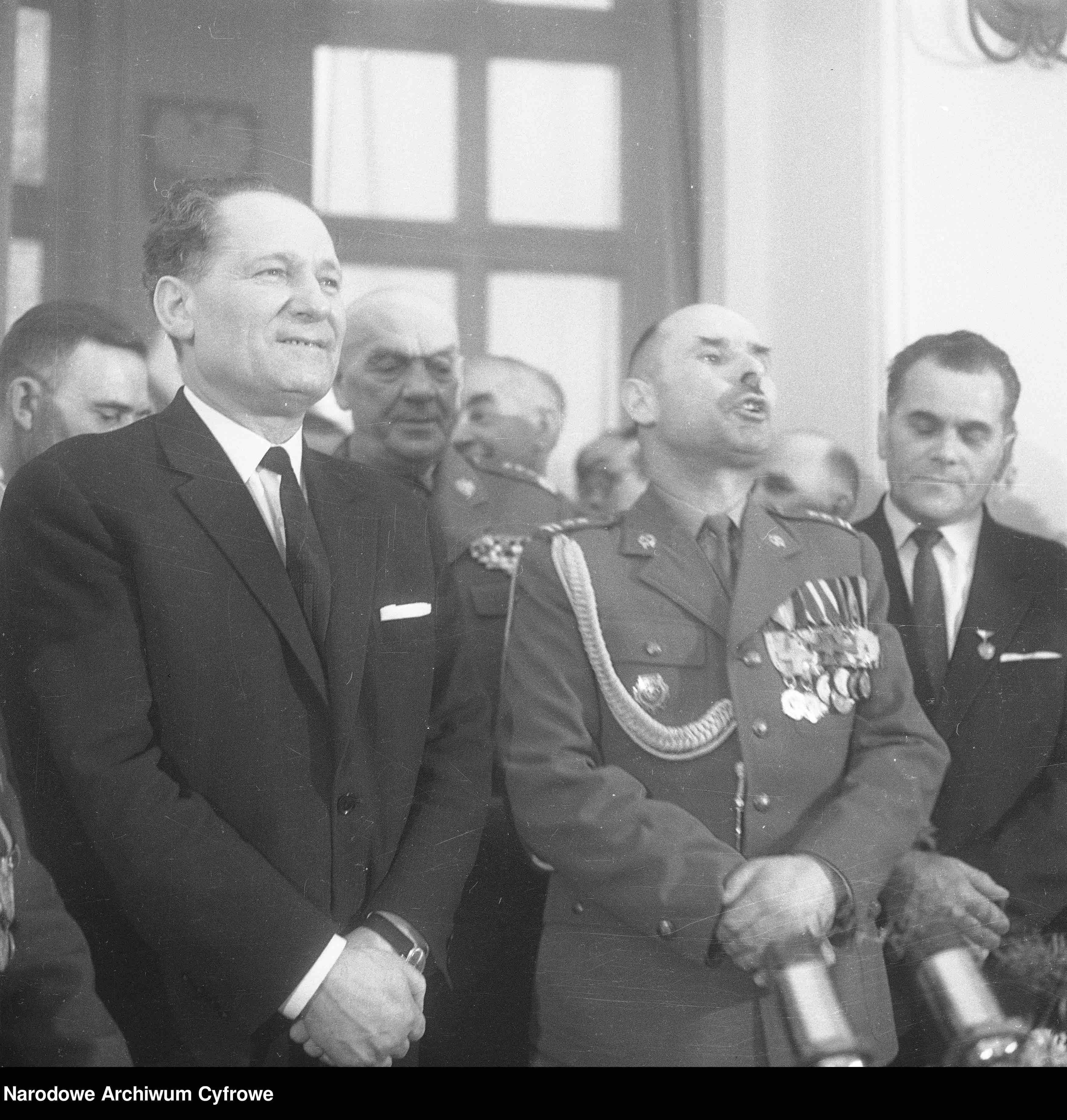 Mieczysław Moczar w garniturze stoi obok oficera w mundurze z medalami.
