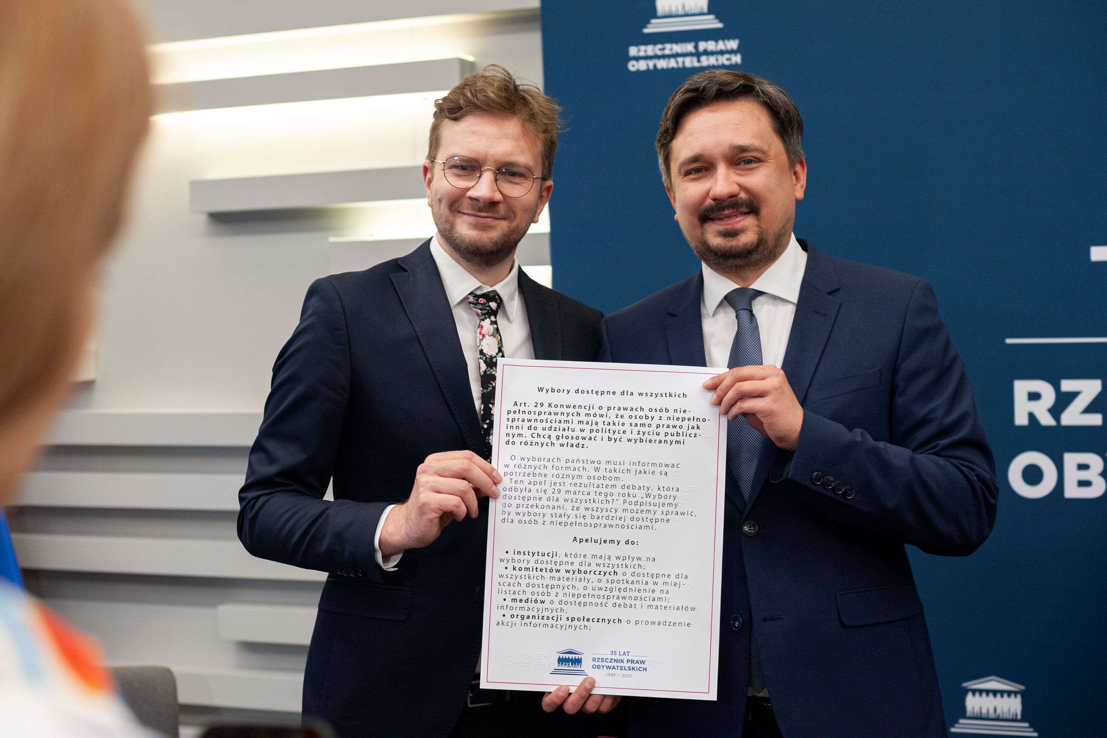 Młody mezczyzna (Bartosz Marganiec) pozuje do zdjęcia z RPO Wiązkiem trzymając apel o dostępne wybory