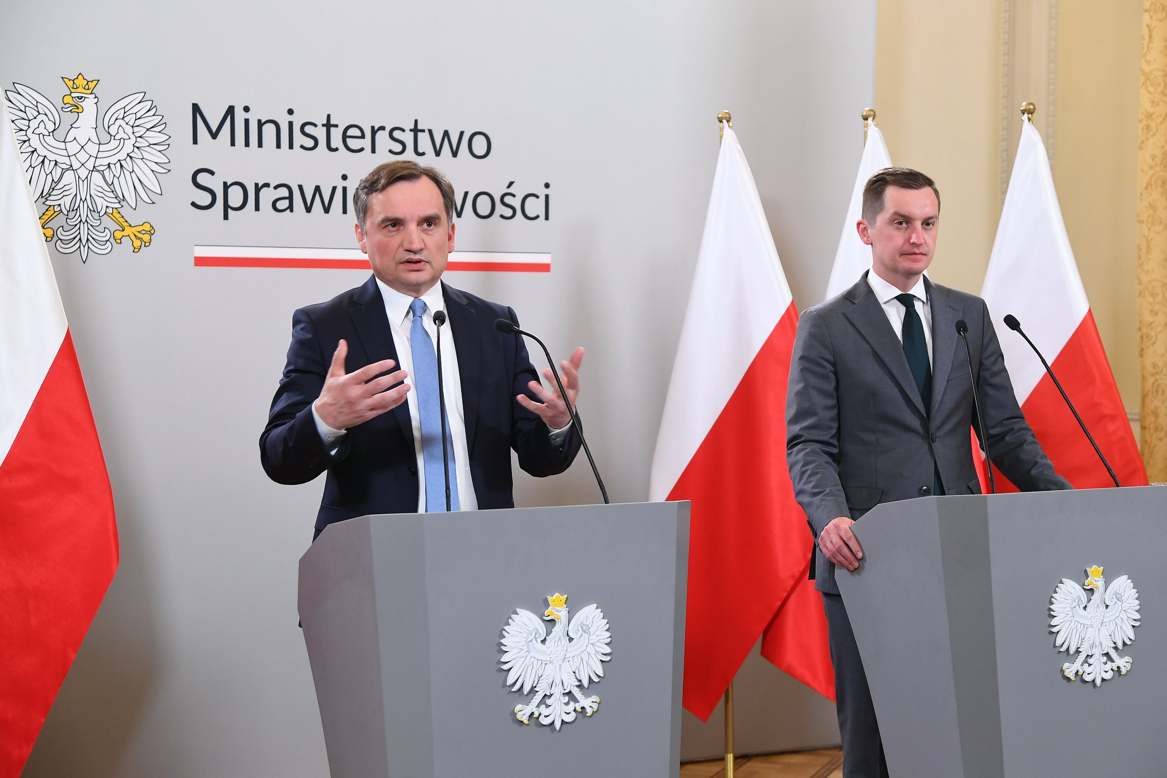 Minister sprawiedliwości Zbigniew Ziobro oraz wiceminister sprawiedliwości Sebastian Kaleta na tle flagi Polski w sali konferencyjnej Ministerstwa Sprawiedliwości komentują wyrok TSUE dotyczący ustawy kagańcowej