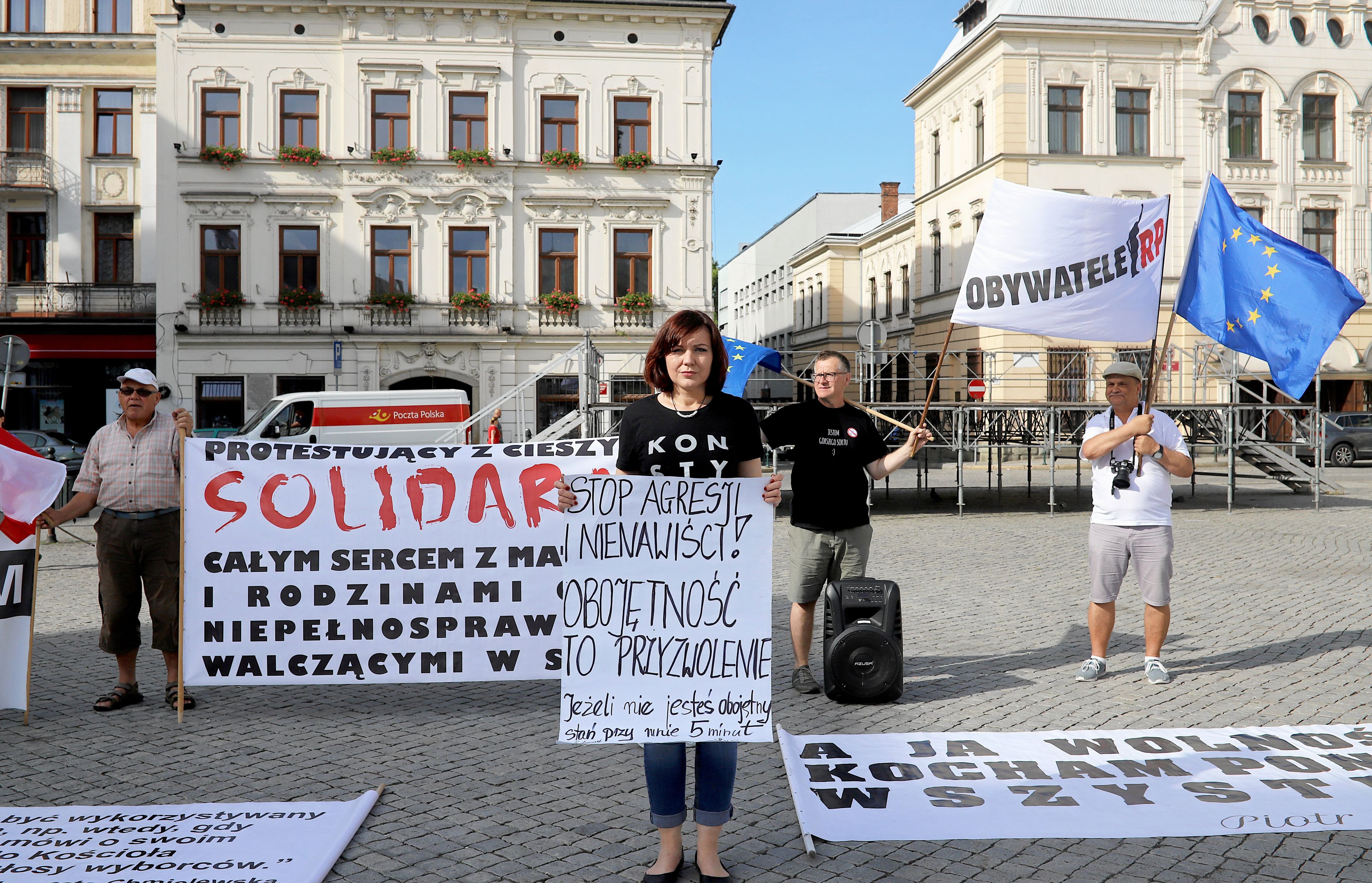 Kobieta stoi z plakatem "Stop ahresji i nienawiści. Obojętnosc to przyzwolenie". Za nią stoją ludzie protestujący w ramach solidarnosci z osobami z niepełnosprawnociami