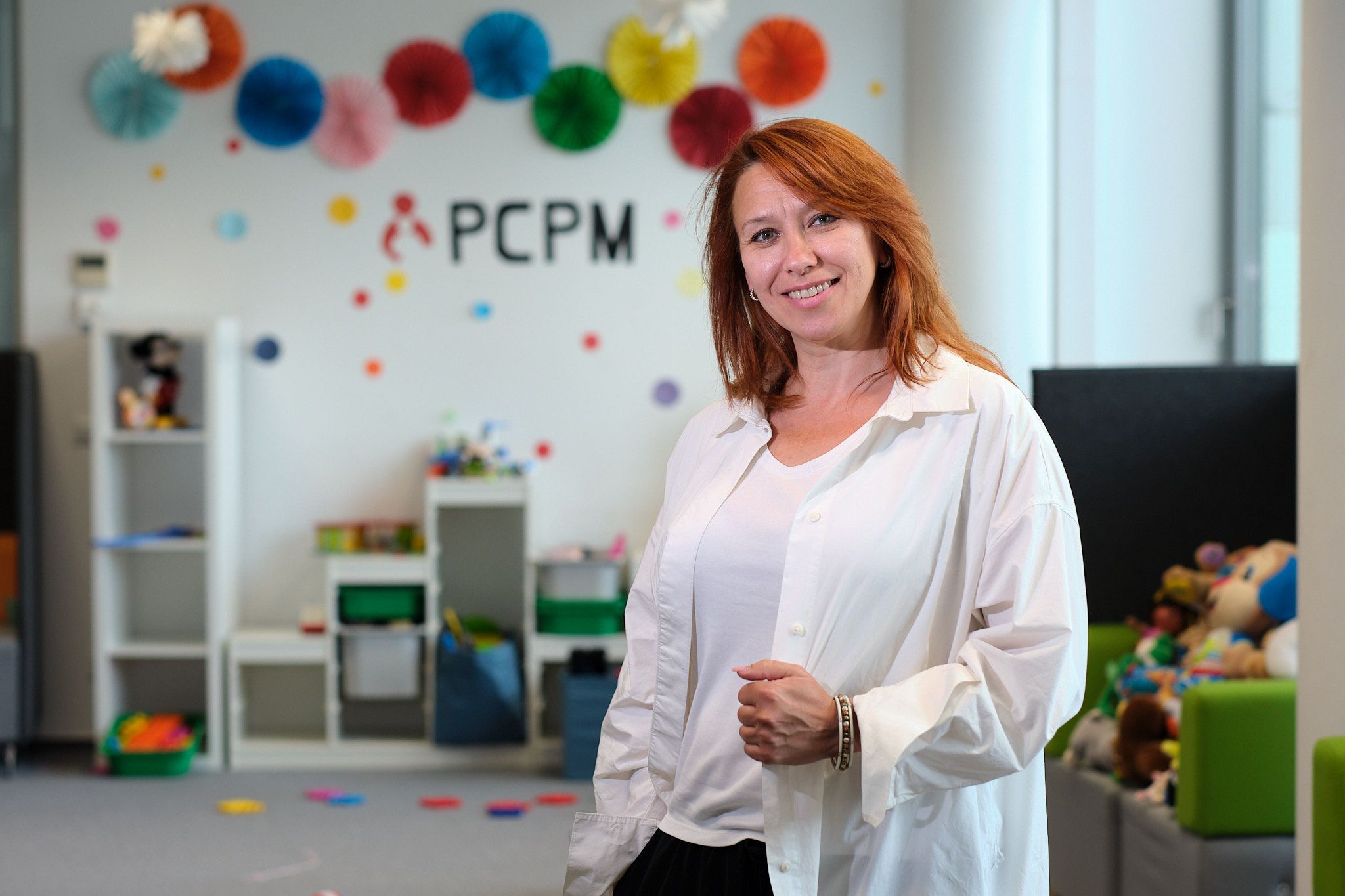 Uśmiechnięta kobieta. W tle ściana przystrojona kolorowymi balonami i napis PCPM