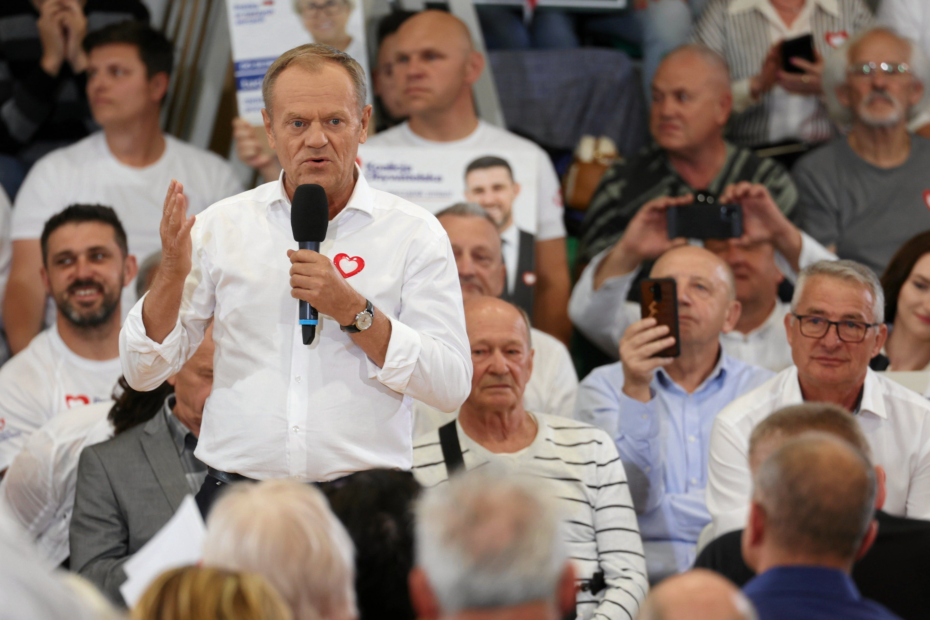 Tusk w białej koszuli, w tle ludzie z telefonami komórkowymi