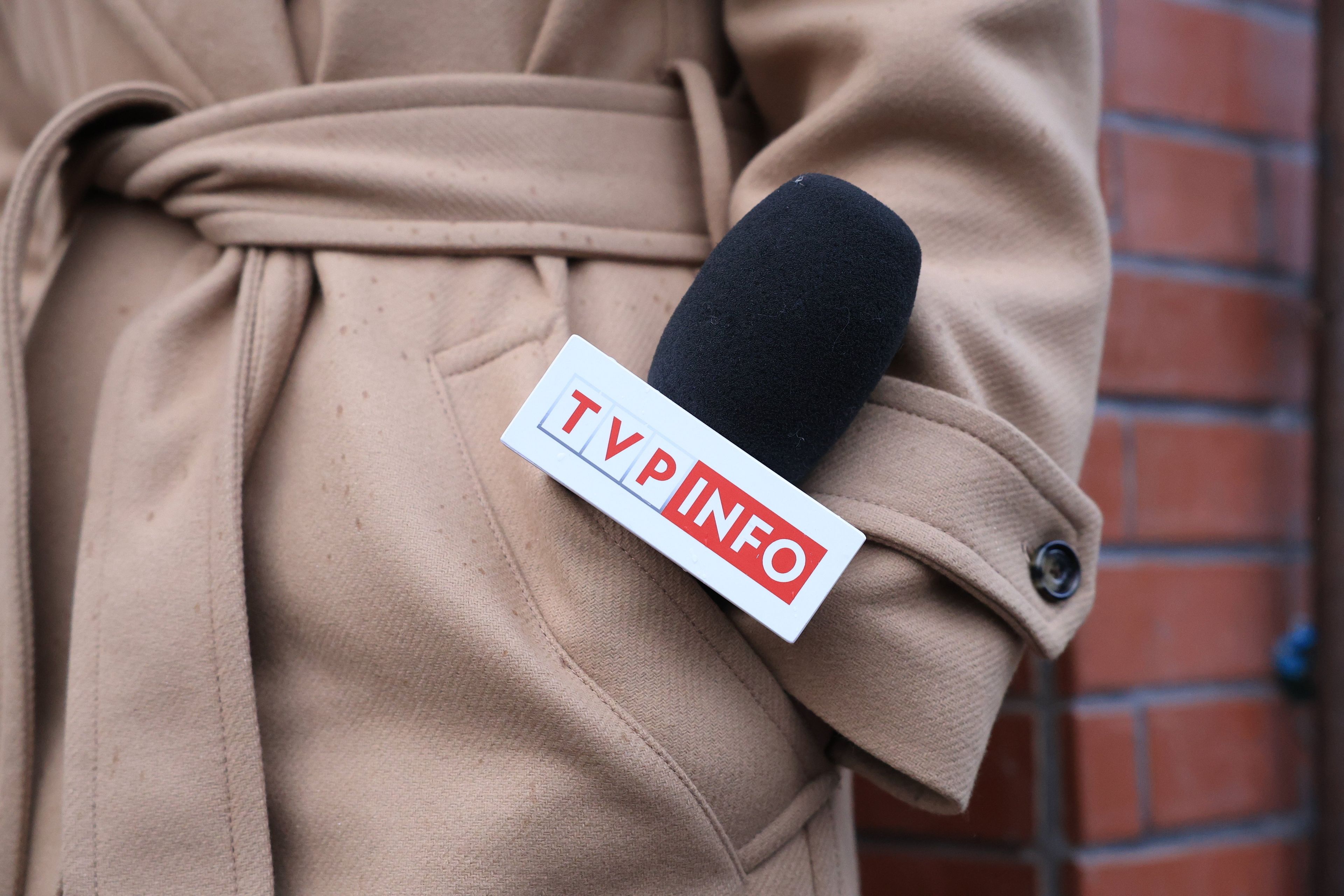 Mikrofon z logo TVP Info w kieszeni jasnego płaszczu reporterki telewizyjnej