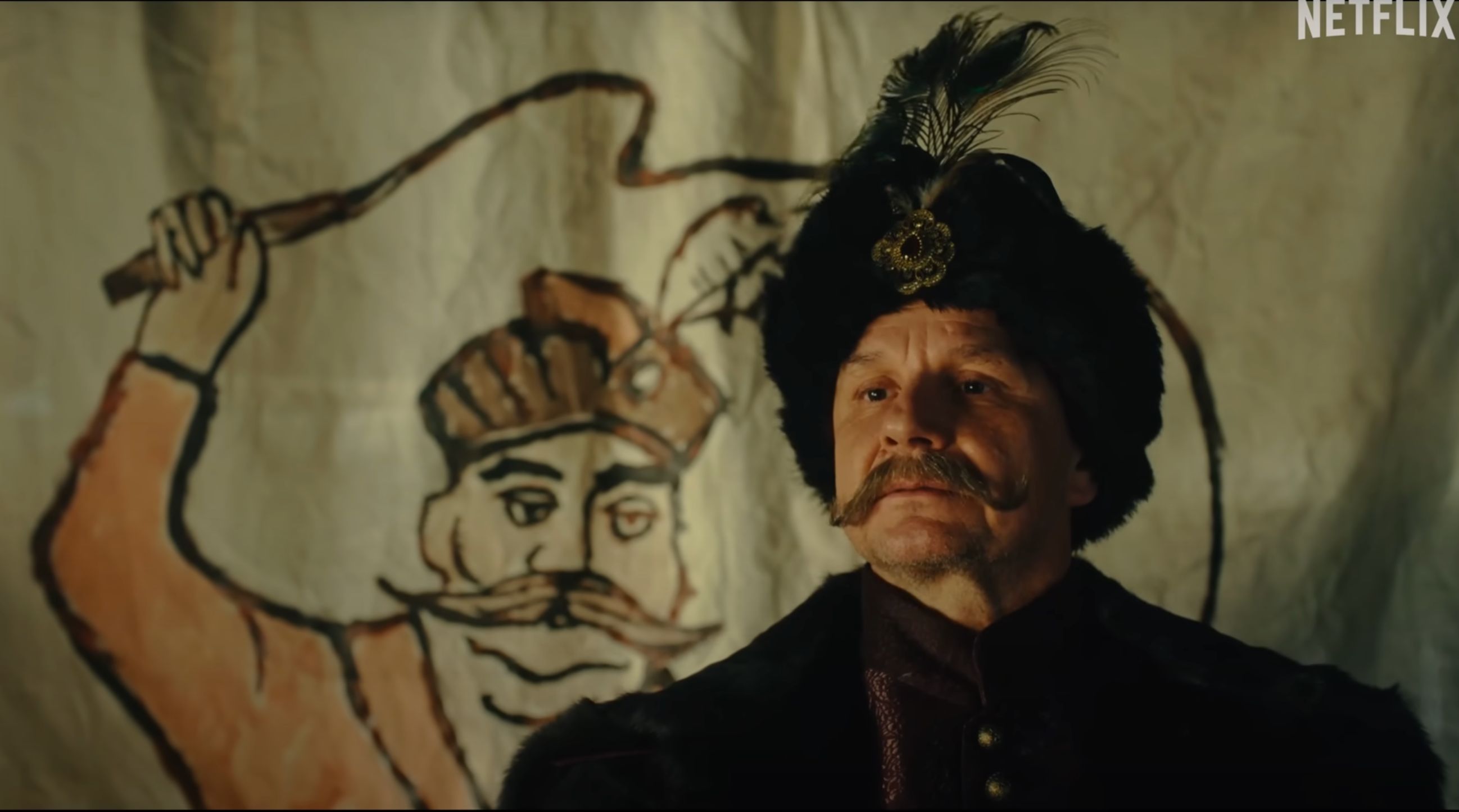 Kadr z serialu Netflix przedstawiający szlachcica Jana Pawła (Bartłomiej Topa) na tle obrazu, przedstawiającego szlachcica z uniesionym pejczem w ręku.