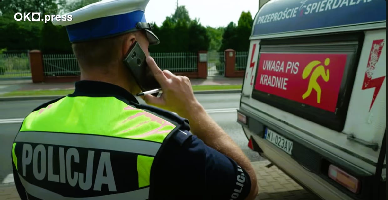 Policjant z komórką przy uchu czyta napis PiS kradnie